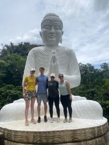 Four grad students standing in front of a large statue of Buddha